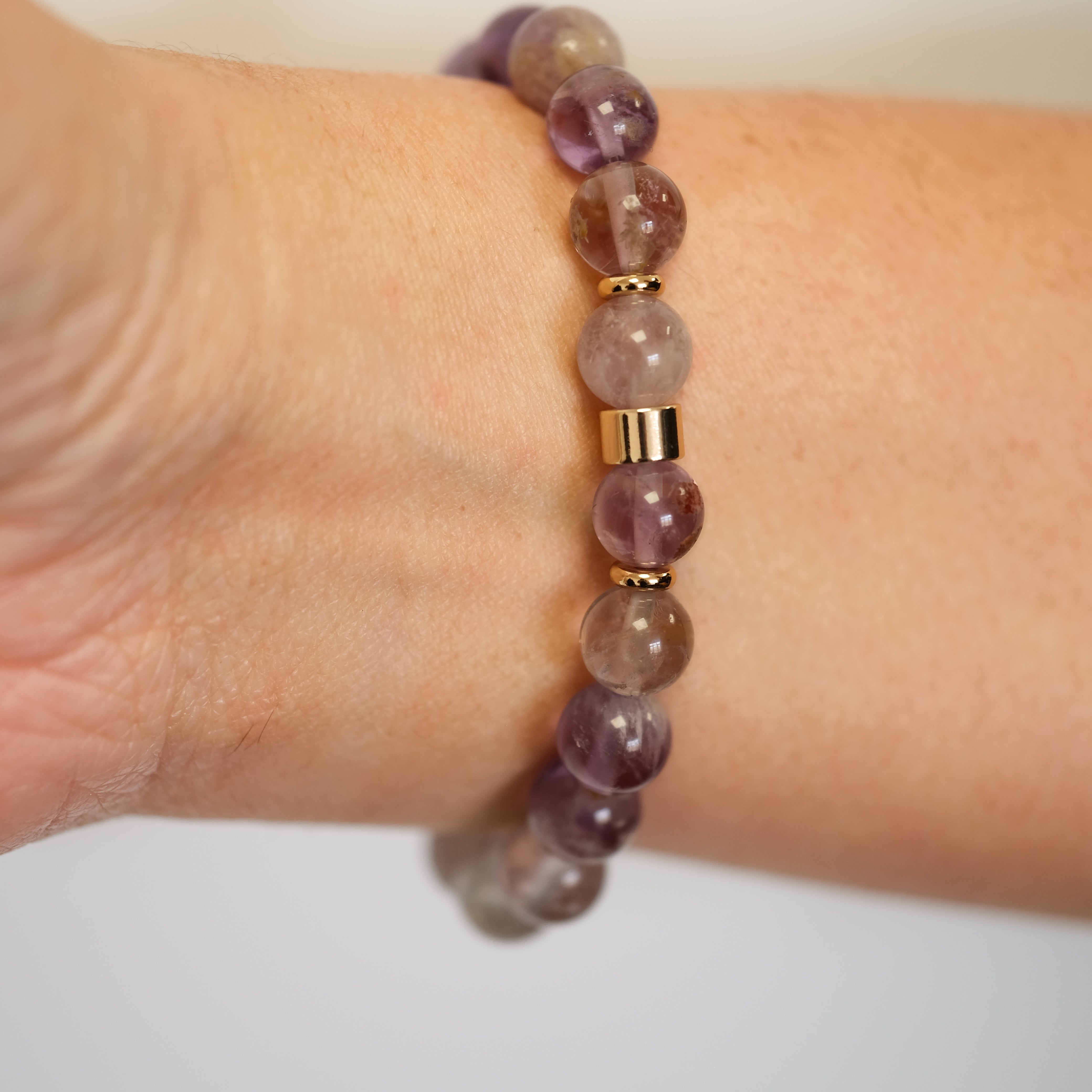 A phantom amethyst gemstone bracelet in 8mm beads worn on a model's wrist from behind