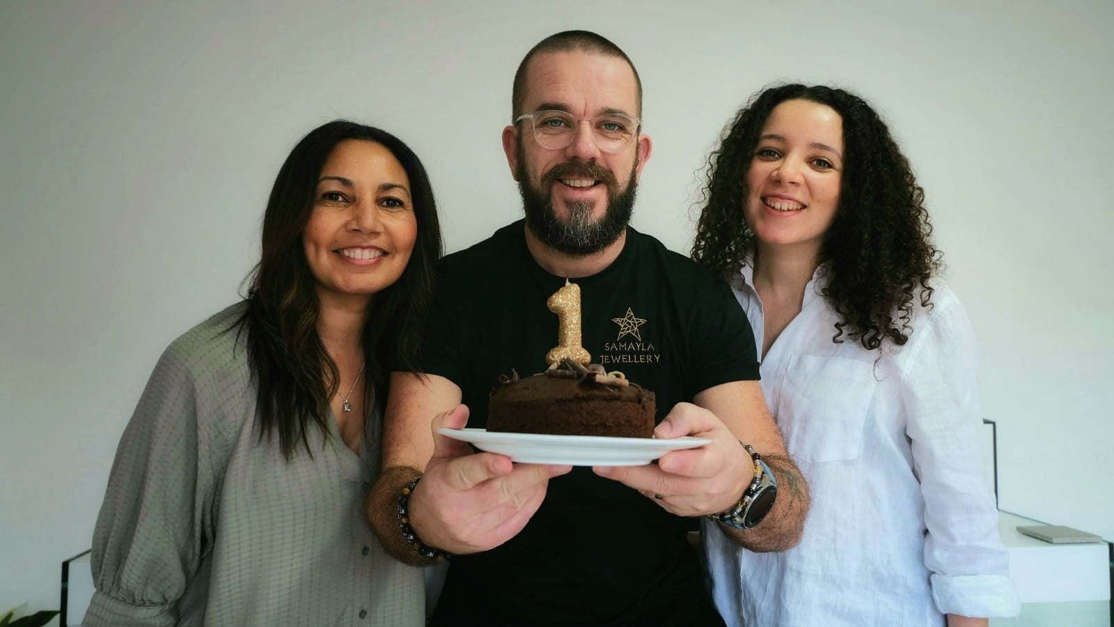 A photo of the Samayla team holding a birthday cake with a '1' candle.