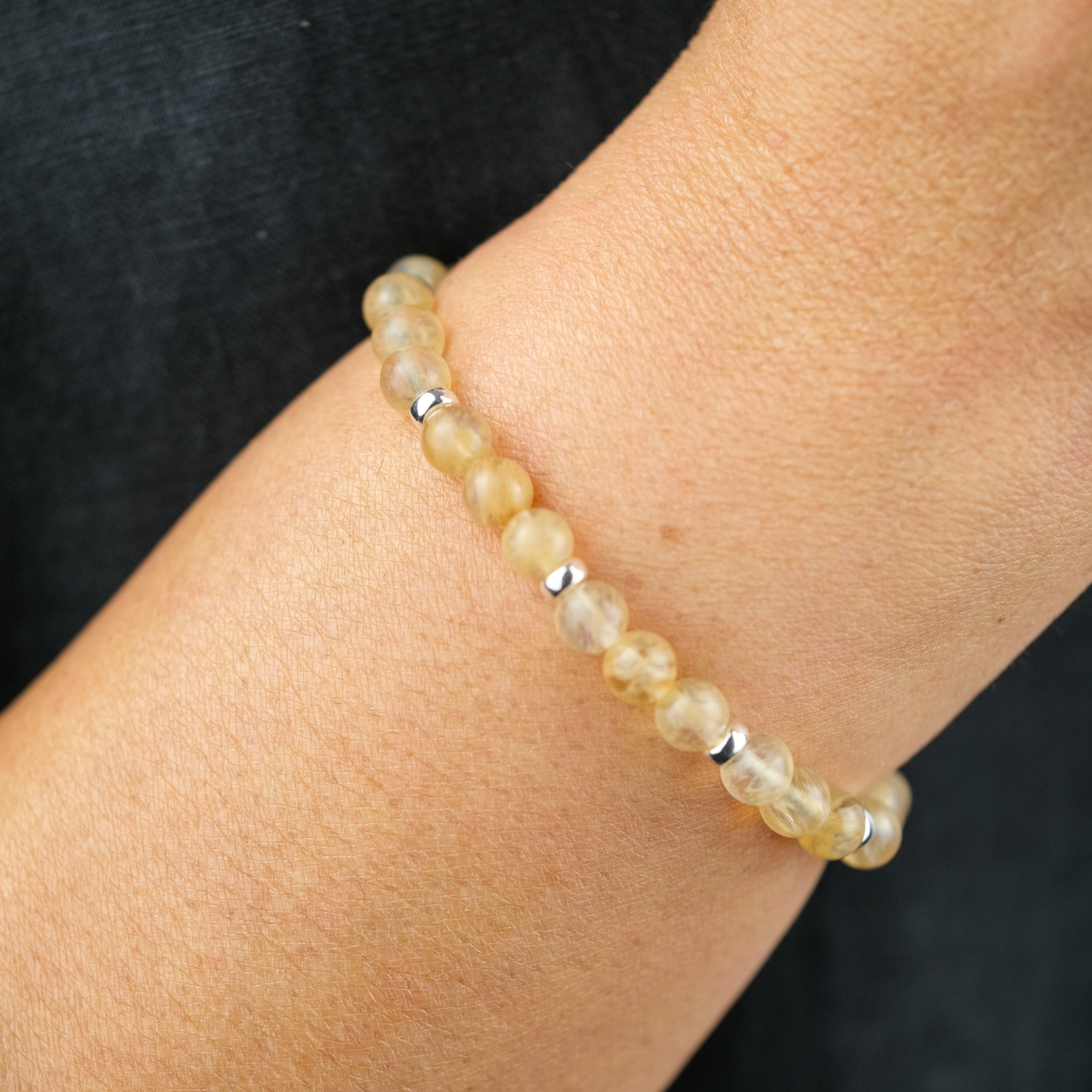 A model wearing a golden healer quartz 6mm gemstone bracelet with silver accessories