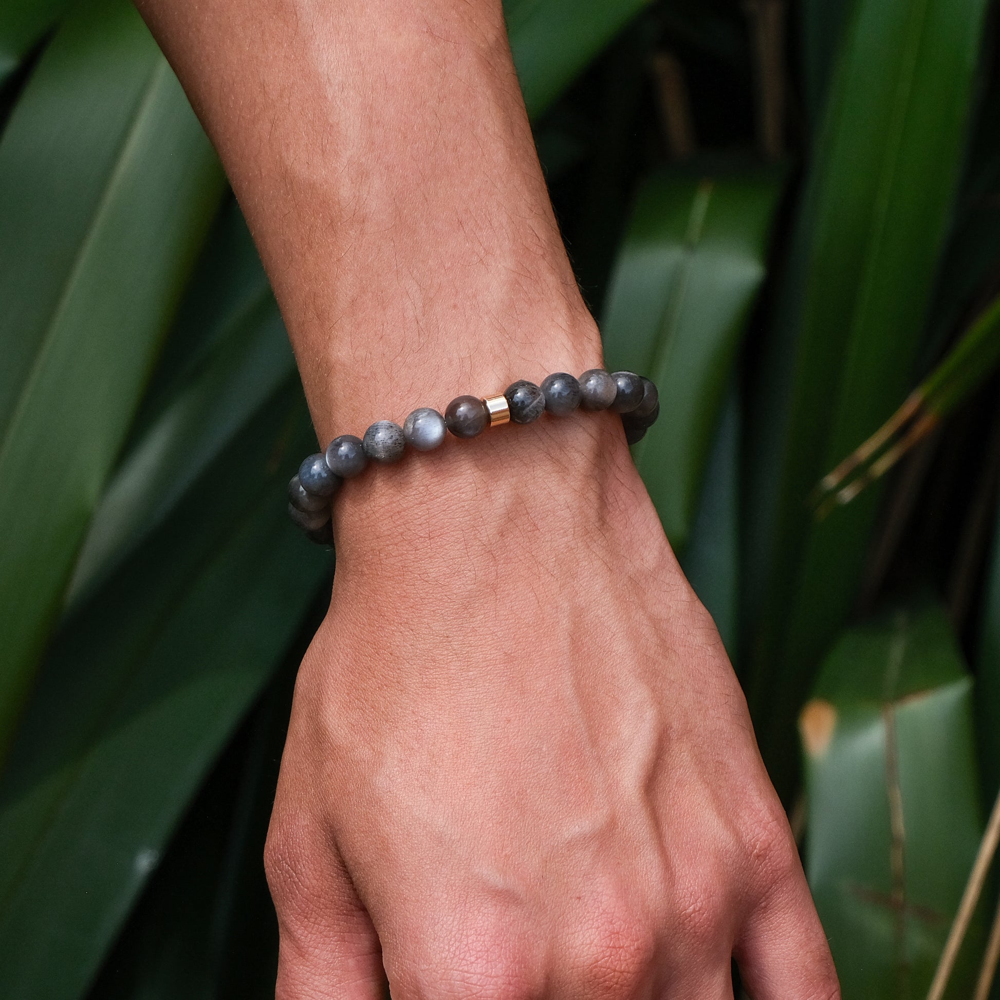 A model wearing a black moonstone gemstone bracelet with gold accessory