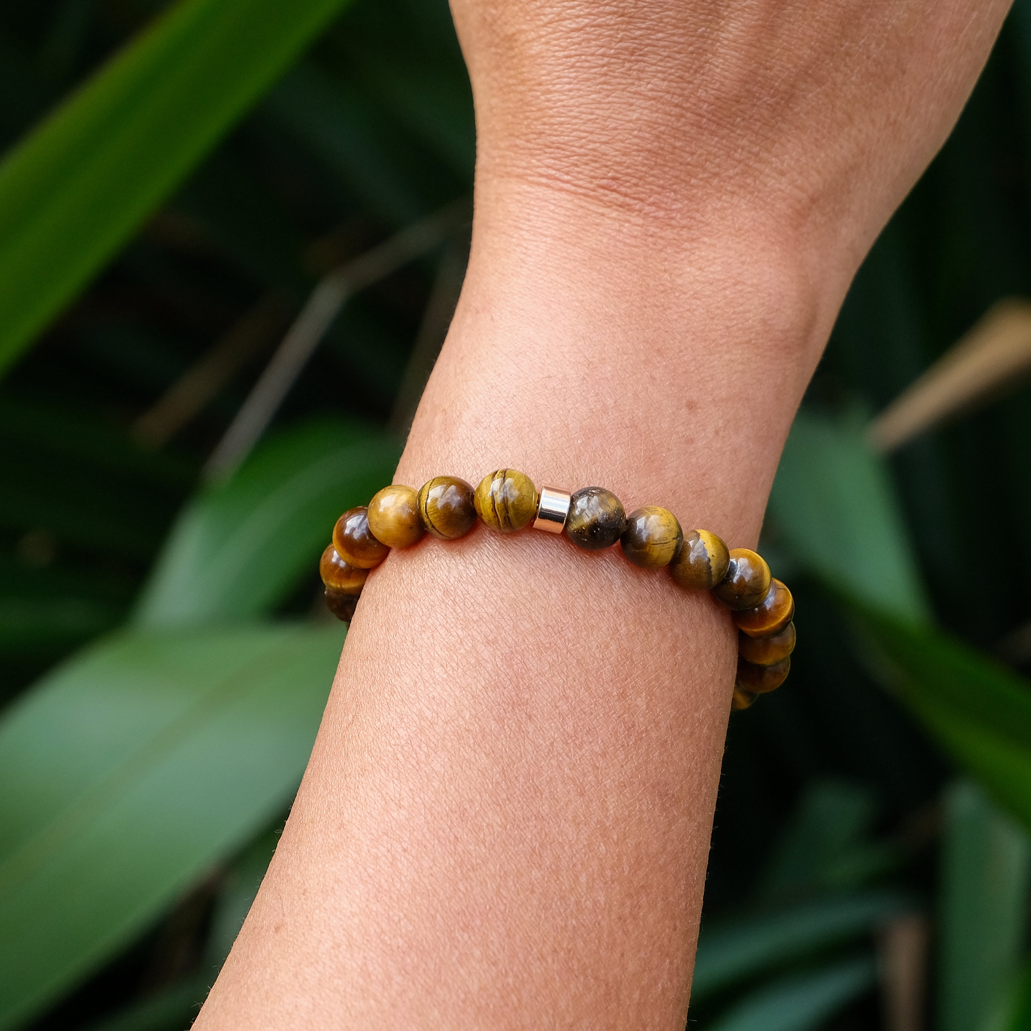 An 8mm tiger eye gemstone bracelet with gold accessory worn on a model's wrist