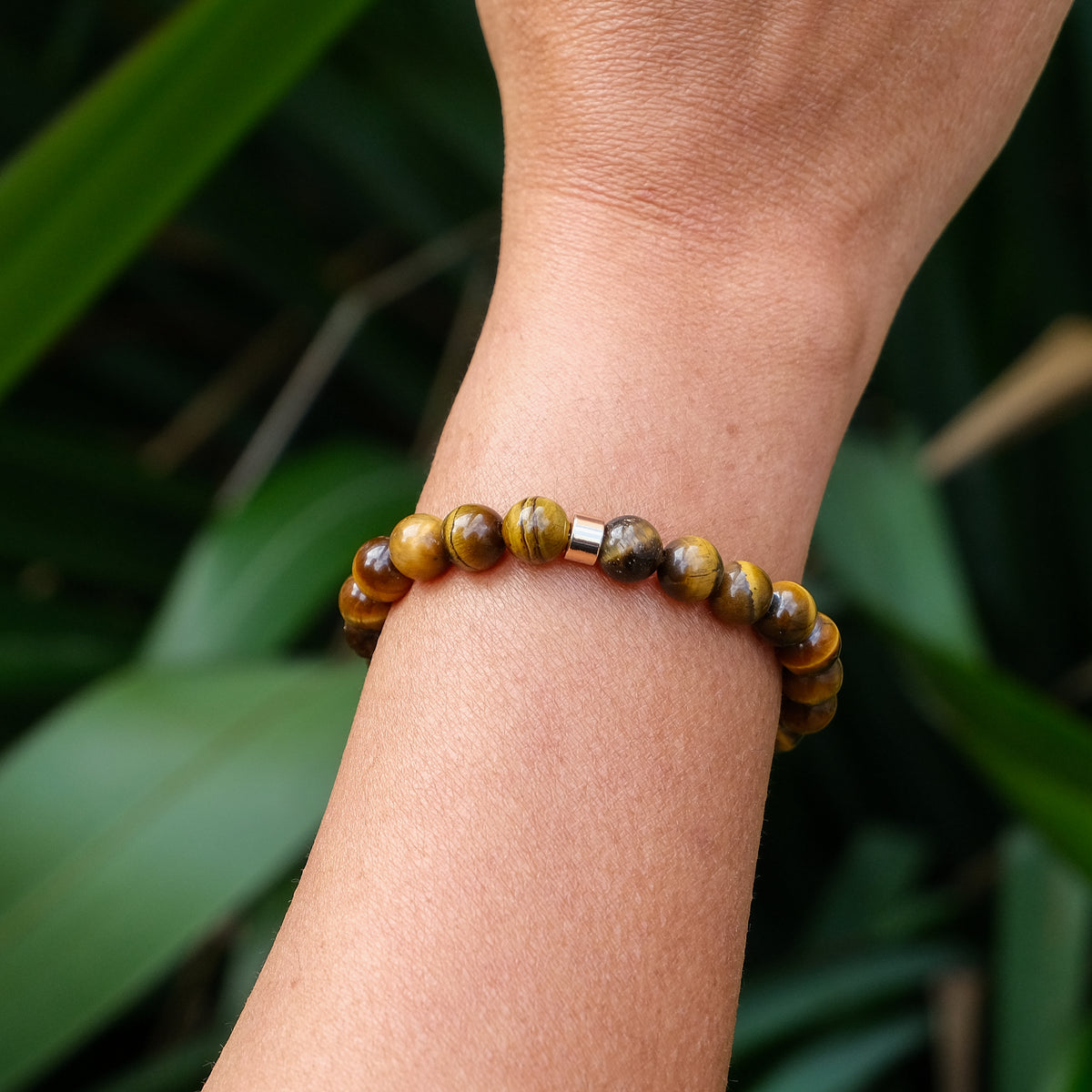 An 8mm tiger eye gemstone bracelet with gold accessory worn on a model's wrist