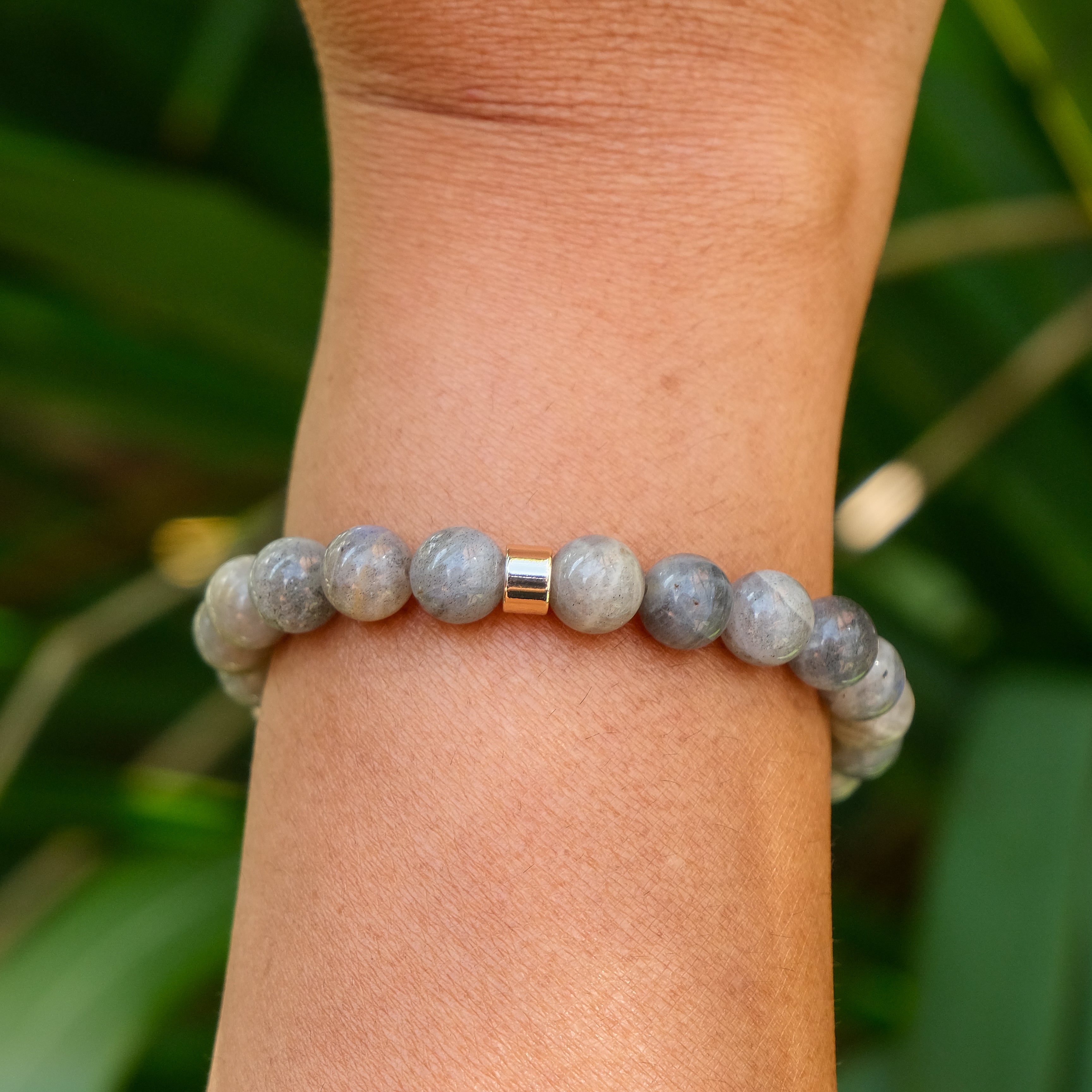 The back of a Labradorite gemstone bracelet with gold accessories worn on a model's wrist