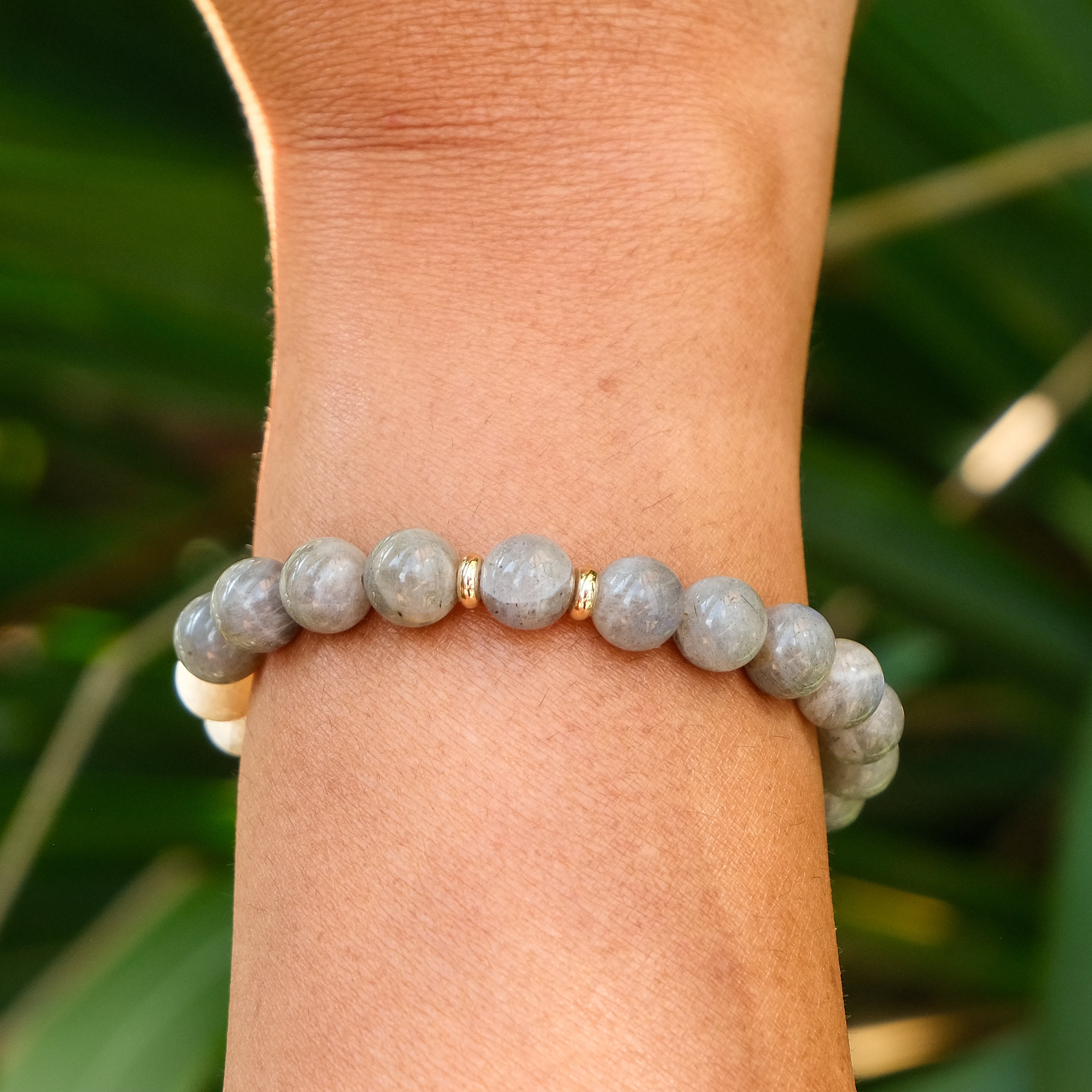 A Labradorite gemstone bracelet with gold accessories worn on a model's wrist