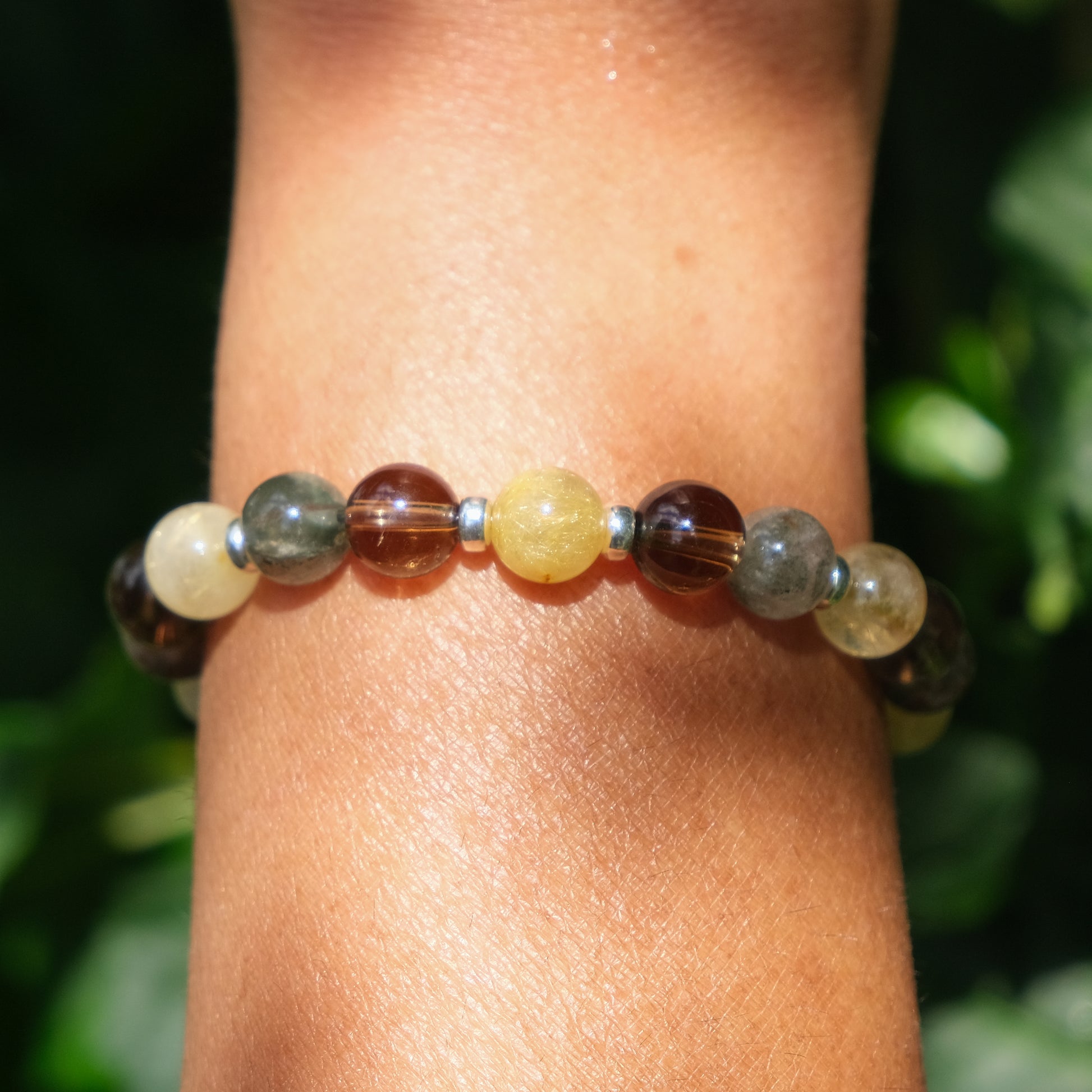 A close up of a model wearing a rutilated quartz, smoky quartz and green phantom quartz bracelet with gold filled accessories
