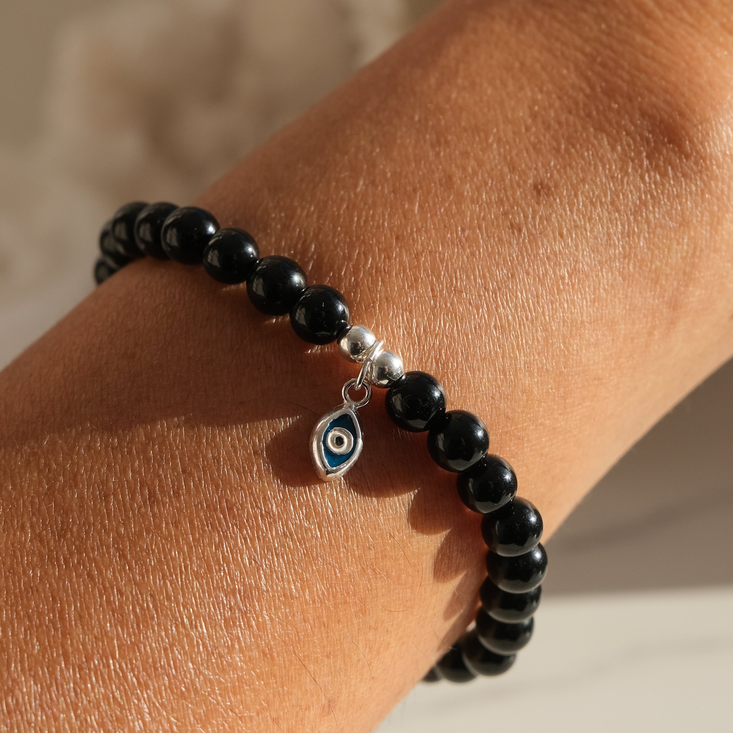 Black onyx gemstone bracelet in 6mm with silver evil eye charm worn by a model