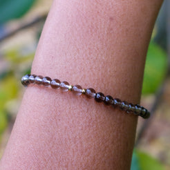4mm smoky quartz gemstone bracelet with gold accessories worn on a model's wrist