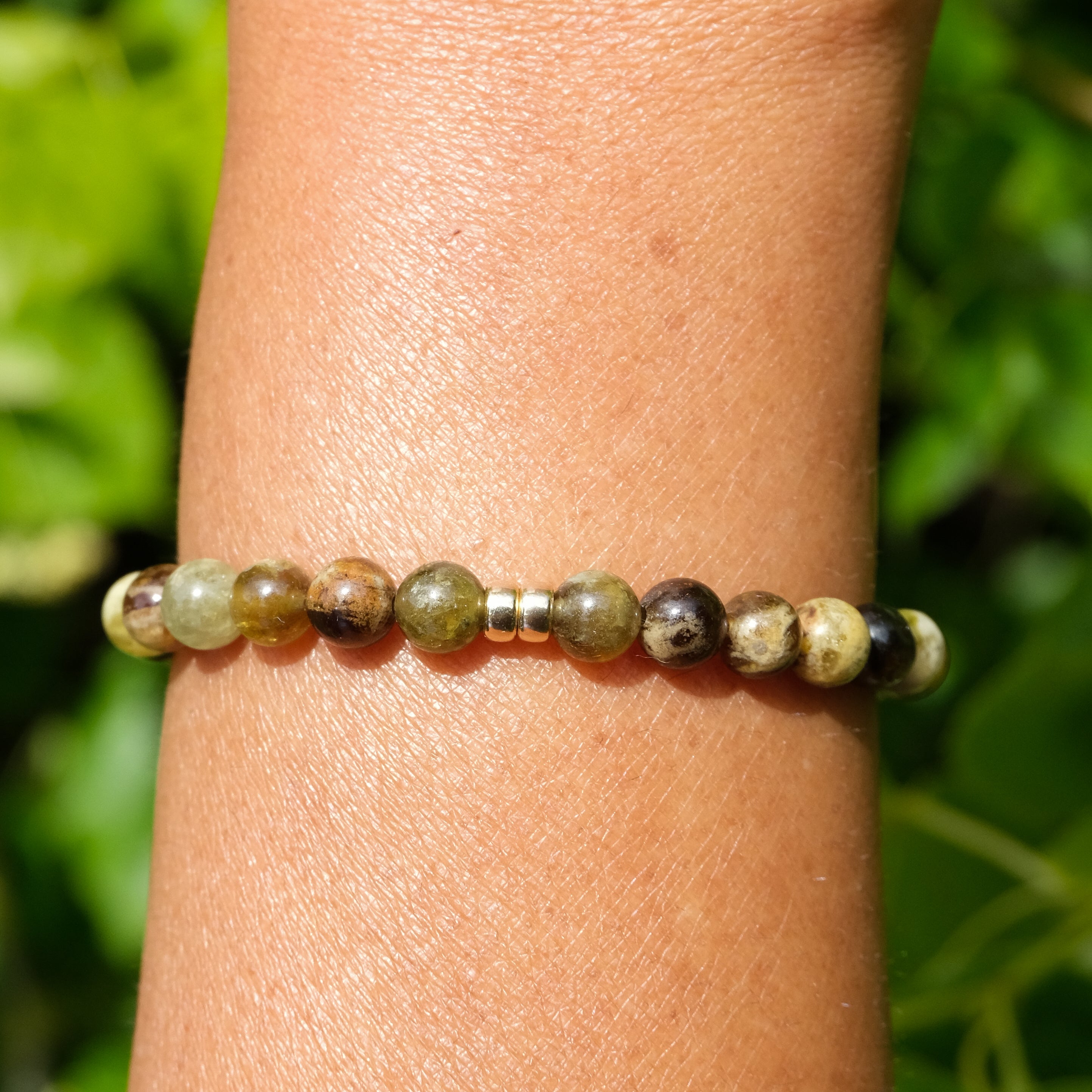 Green garnet gemstone bracelet in 6mm with gold accessories worn on a model's wrist
