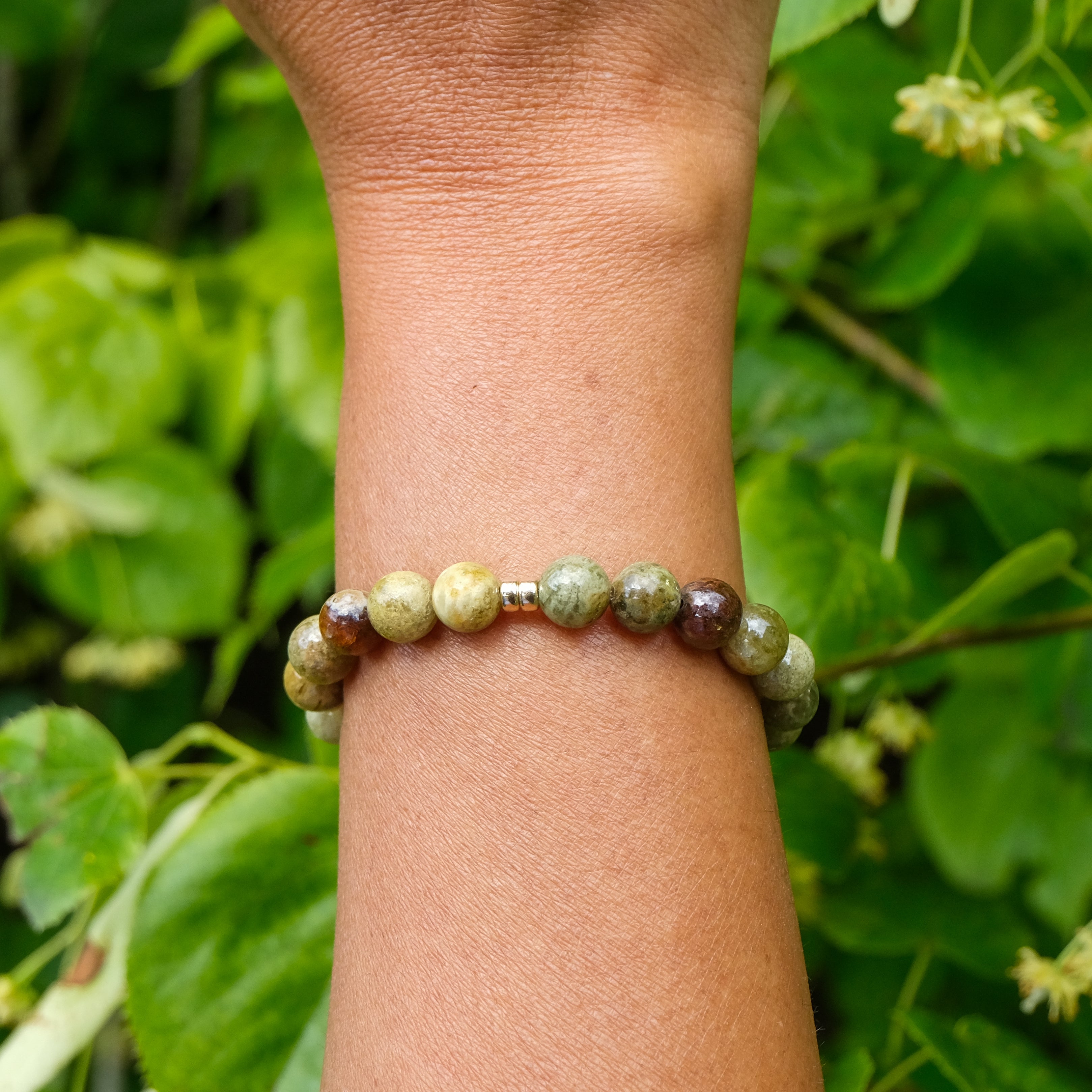 Green garnet gemstone bracelet in 8mm with gold accessories worn on a model's wrist