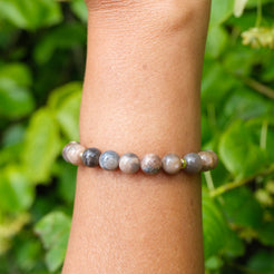 Black moonstone and sunstone gemstone bracelet with gold accessories worn on a model's wrist