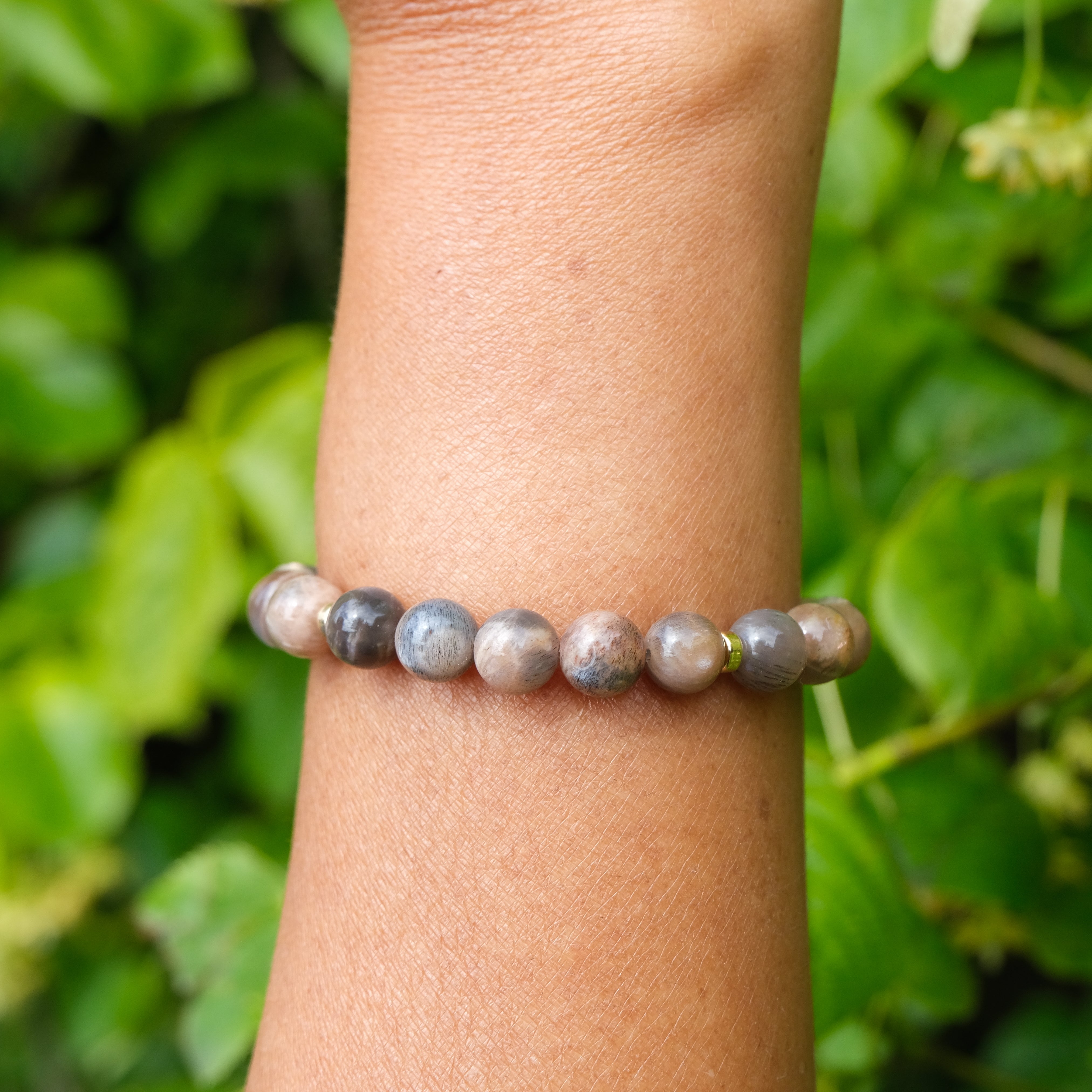 Black moonstone and sunstone gemstone bracelet with gold accessories worn on a model's wrist