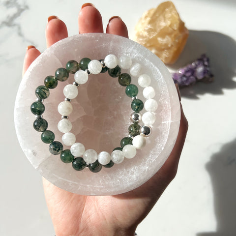 A selenite bowl held in a hand with crystal bracelets inside it