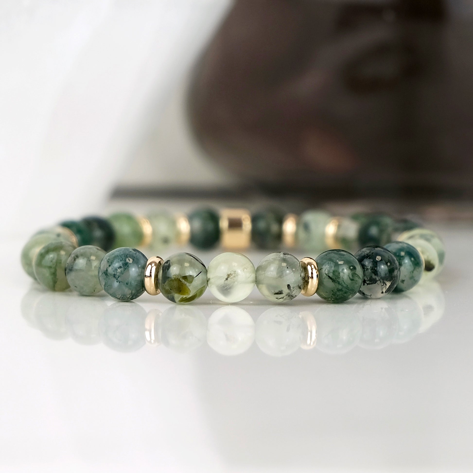 Moss Agate and Prehnite gemstone bracelet in 6mm beads with gold accessories. The bracelet is on a reflective white tile.