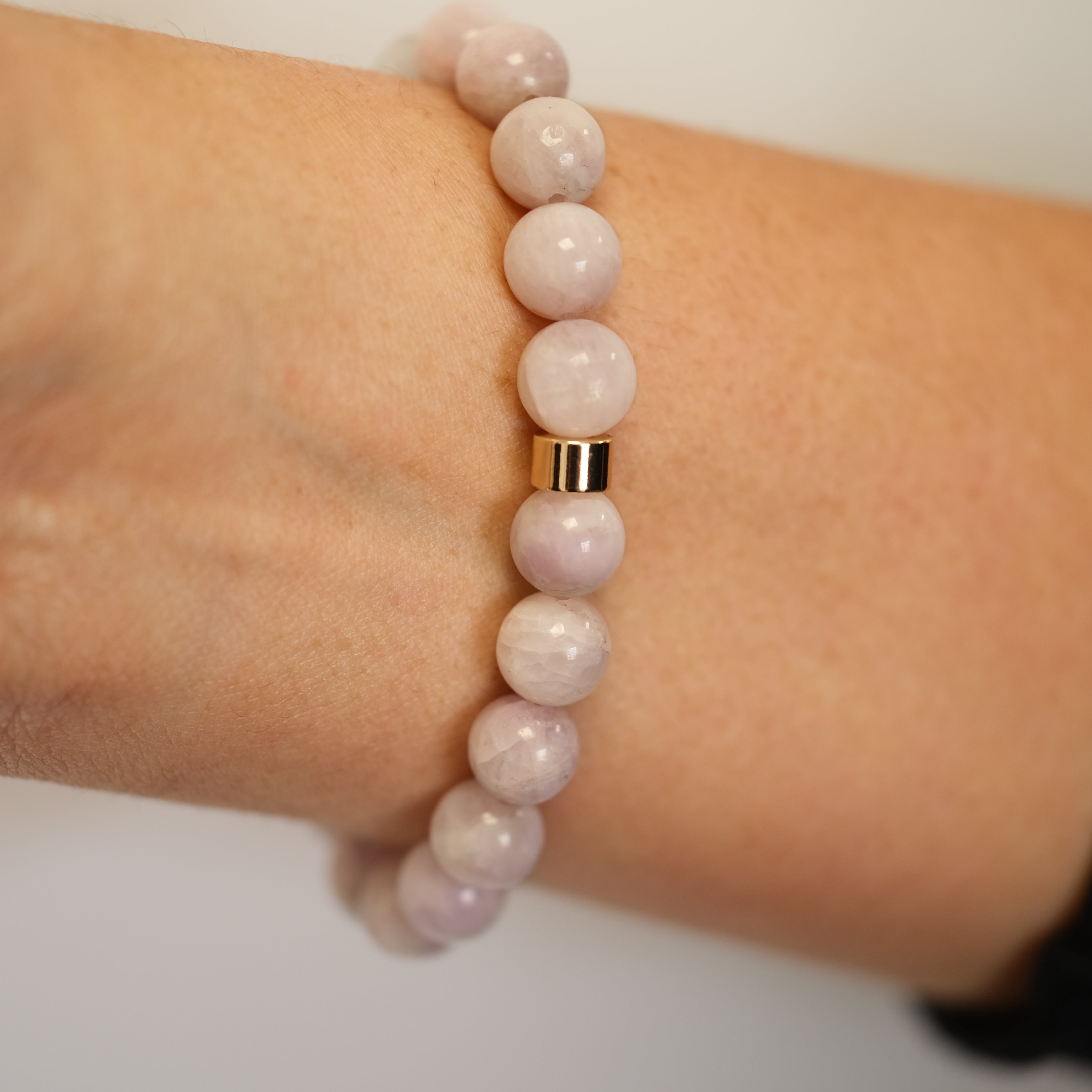 A Kunzite gemstone bracelet with gold accessories worn on a model's wrist from the back