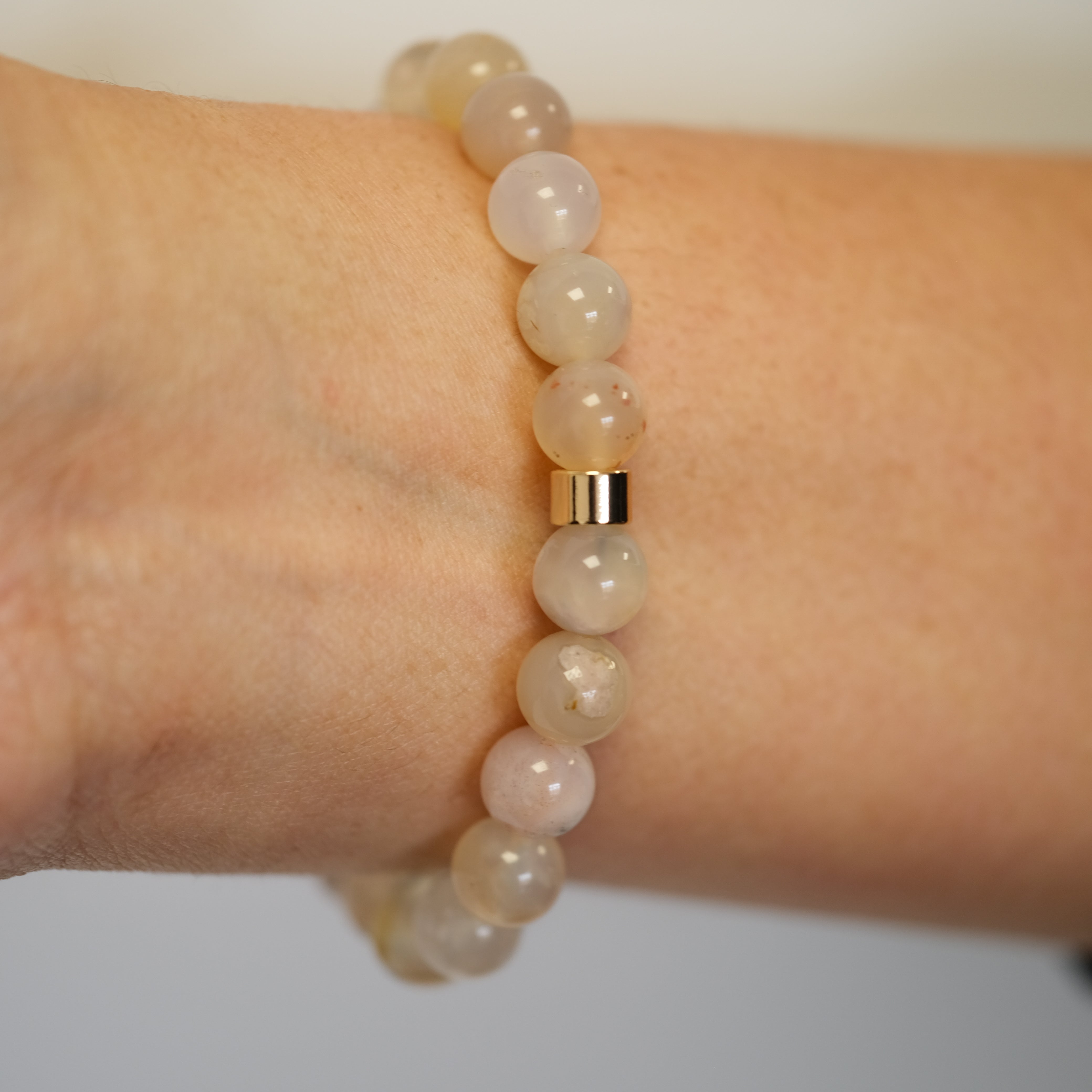 A Flower Blossom Agate gemstone bracelet with gold accessories on a model's wrist from the back