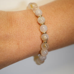 A Flower Blossom Agate gemstone bracelet with gold accessories on a model's wrist