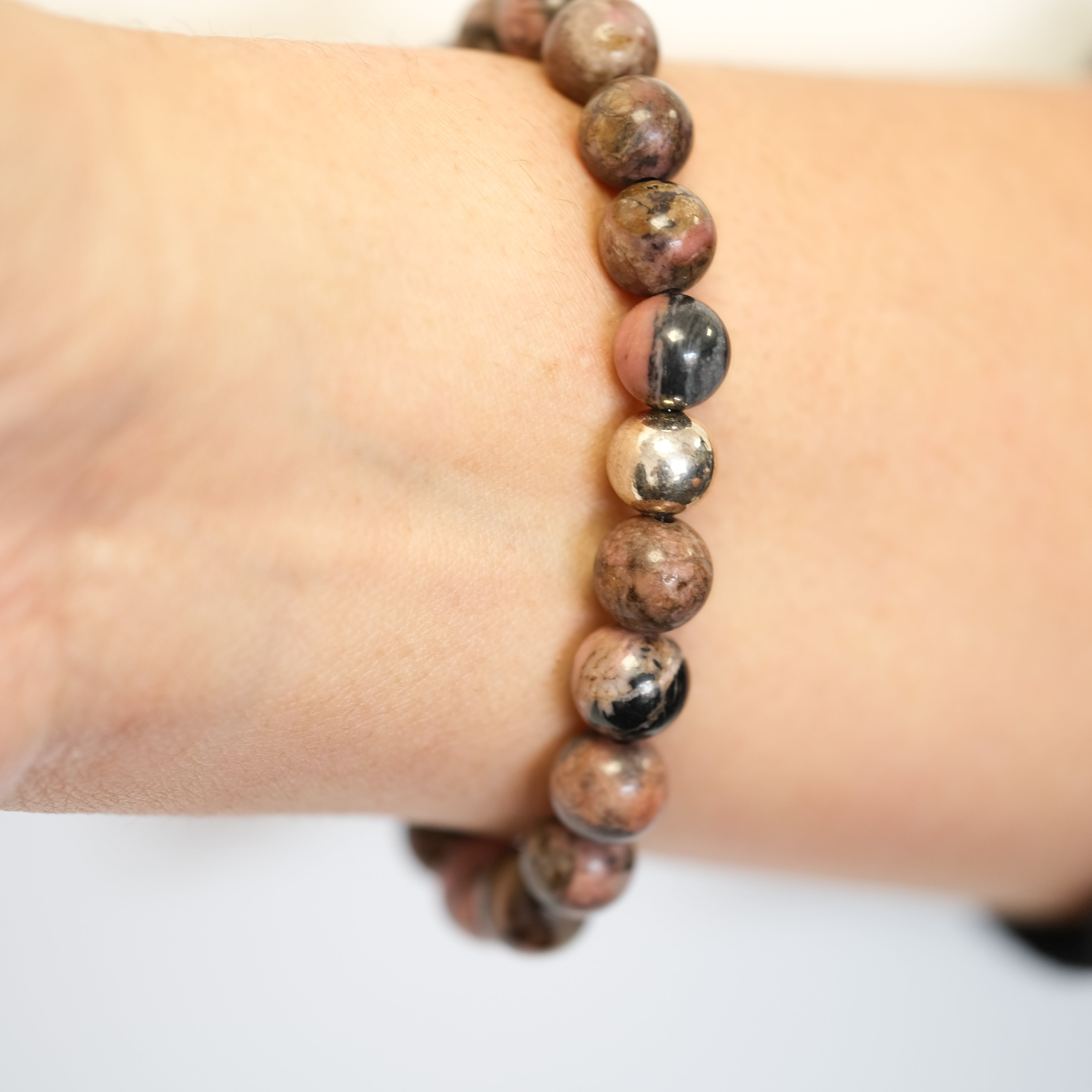 A Rhodonite gemstone bracelet with gold accessories worn on a model's wrist from behind