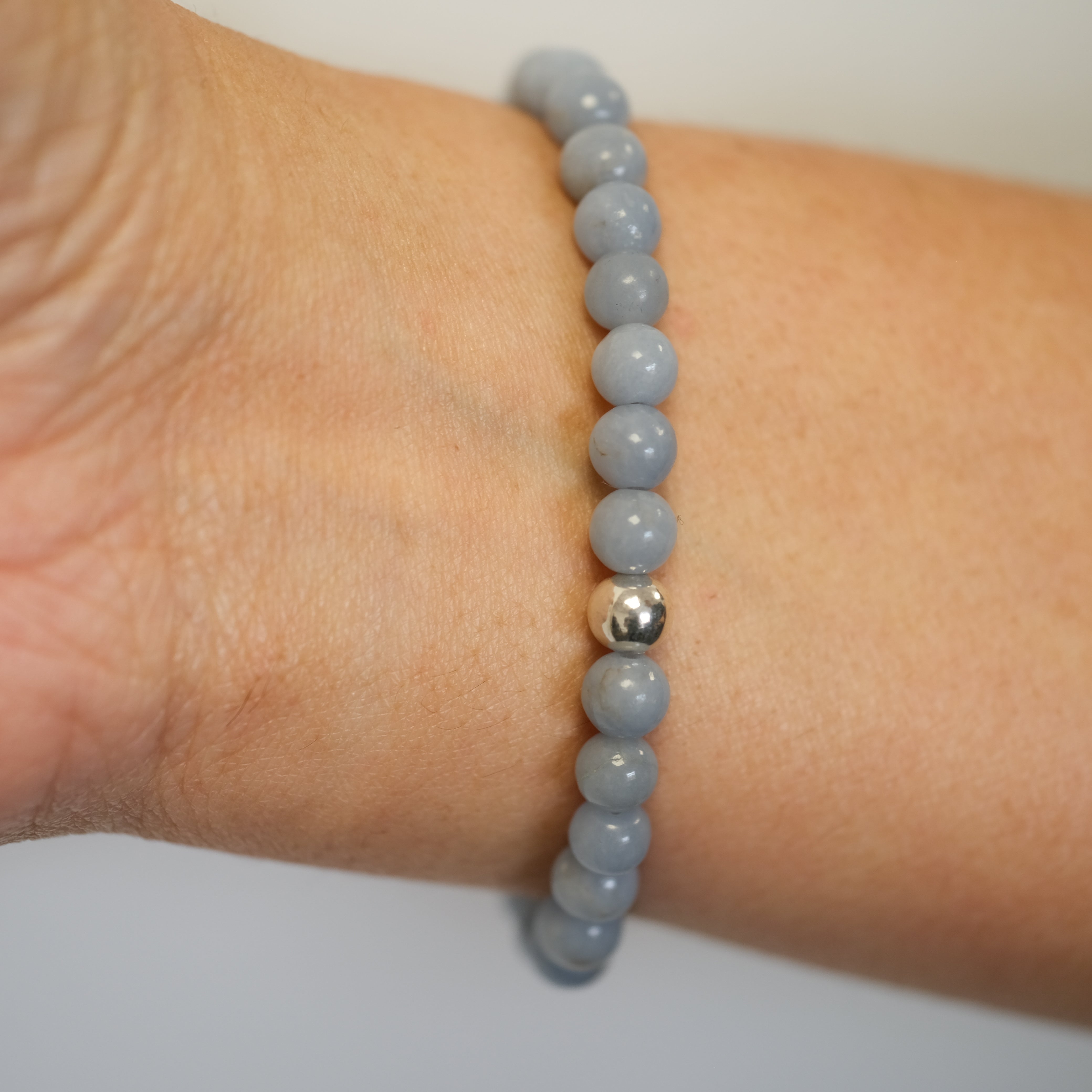 Angelite gemstone bracelet with silver accessories worn on a model's wrist from behind
