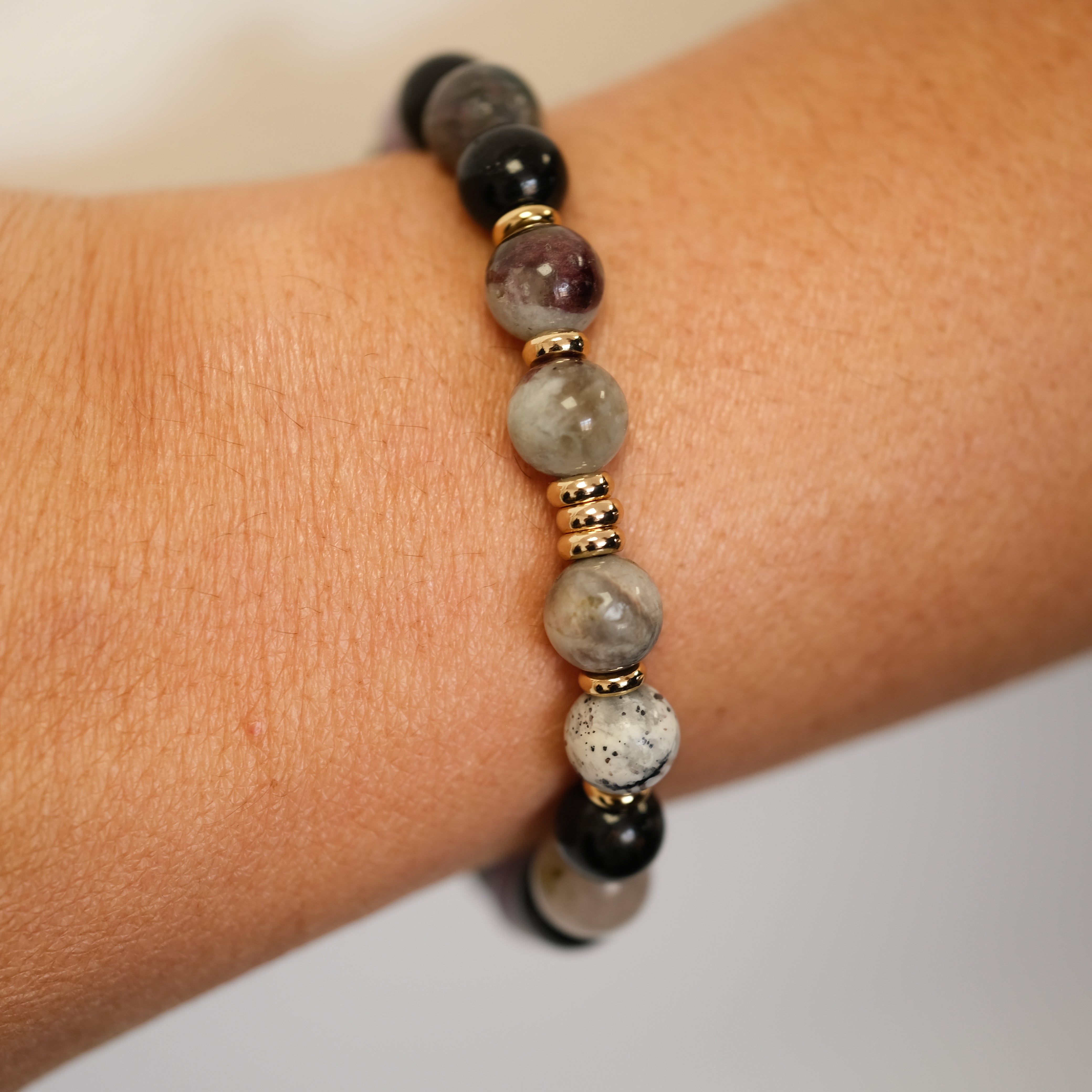 A multi-coloured tourmaline bracelet with gold accessories worn on a model's wrist