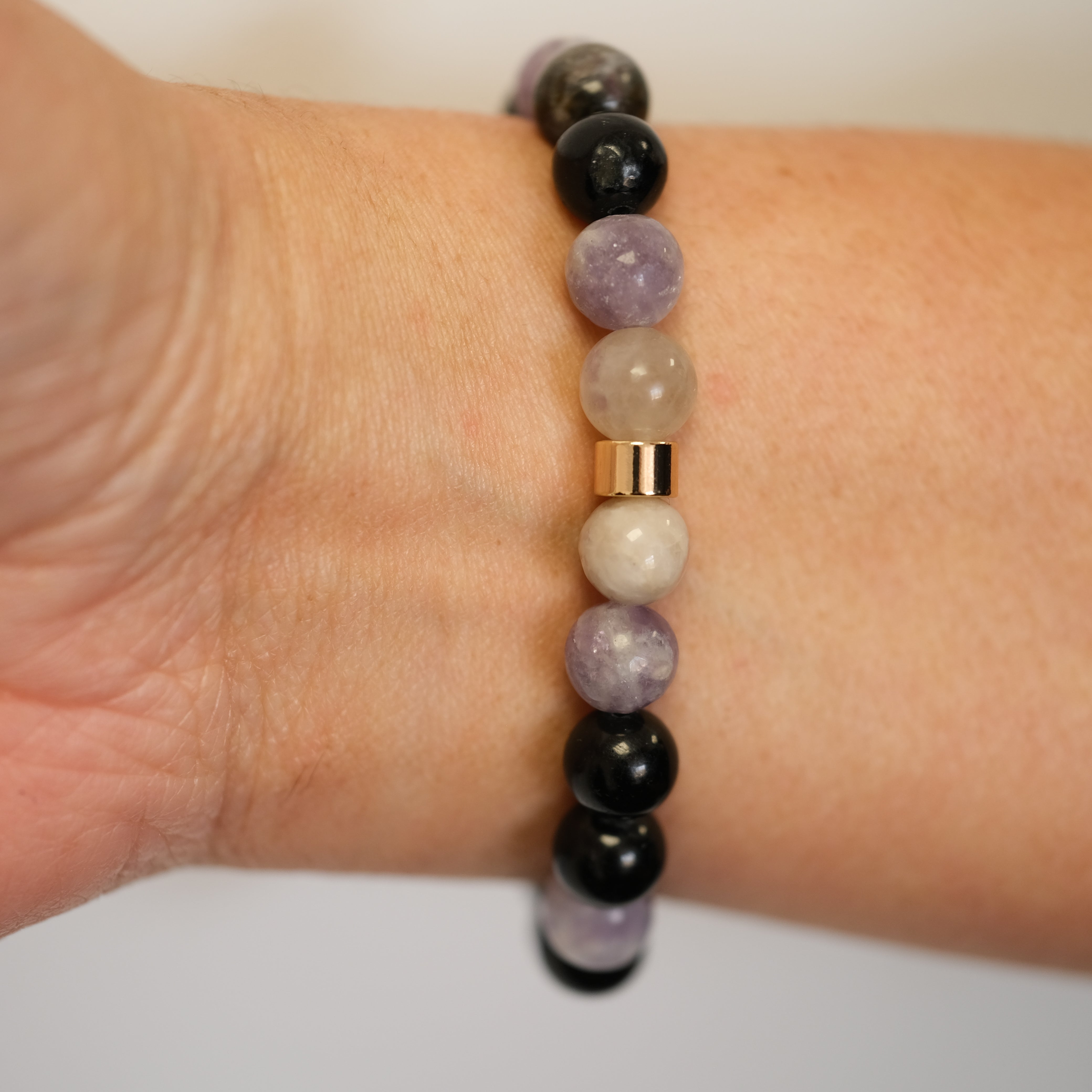 A multi-coloured tourmaline bracelet with gold accessories worn on a model's wrist from behind