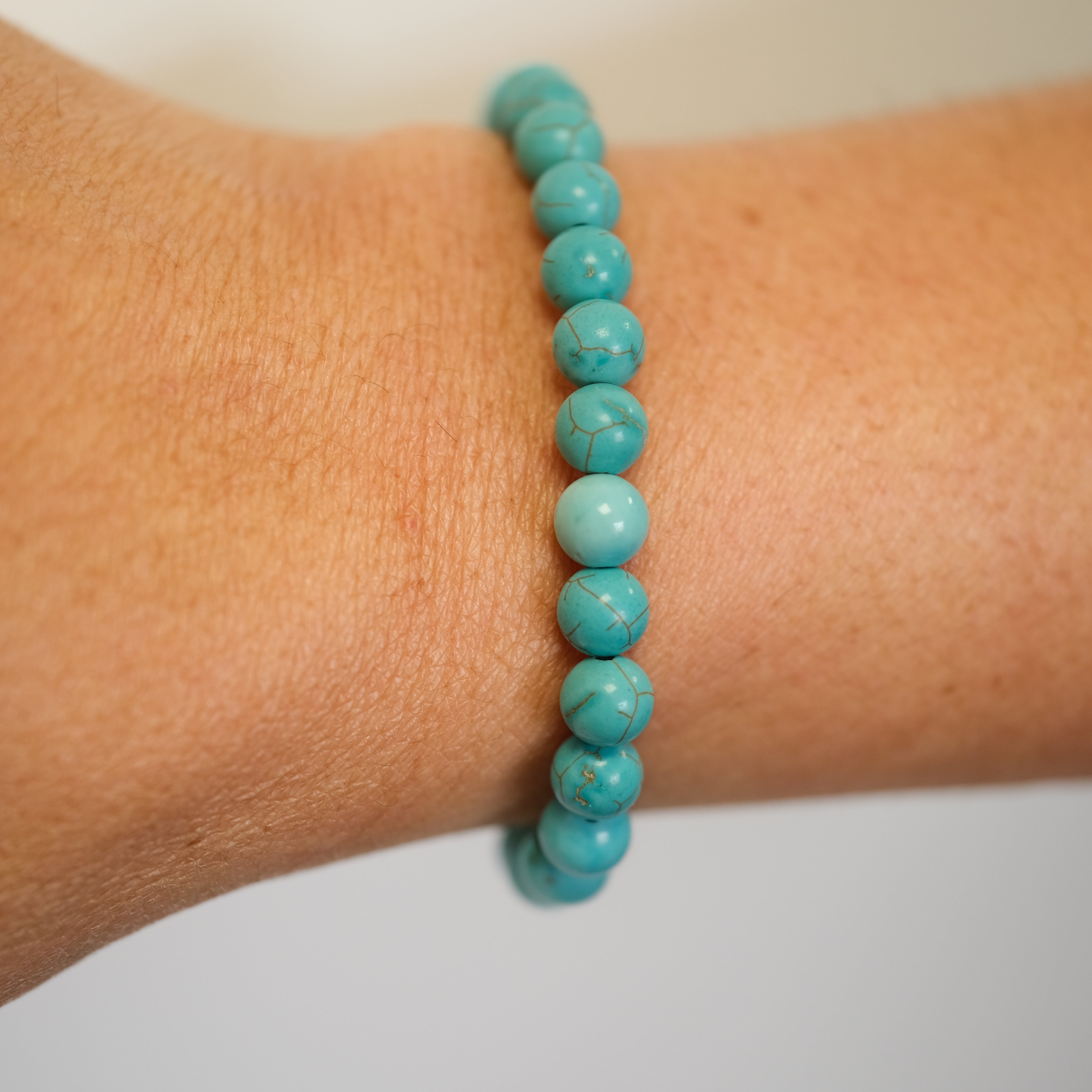 A turquoise gemstone bracelet in 6mm beads worn on a model's wrist