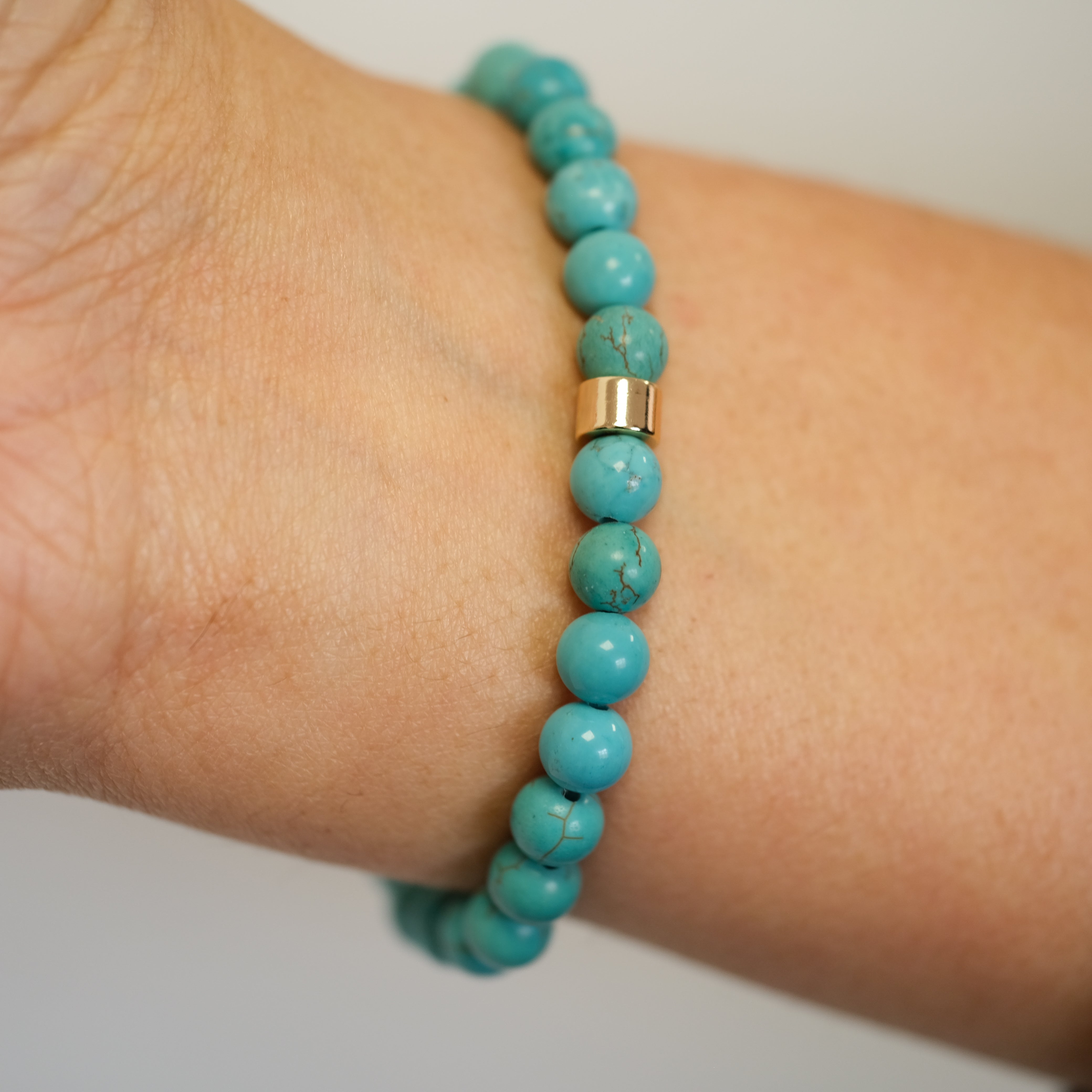 A turquoise gemstone bracelet in 6mm beads worn on a model's wrist from behind