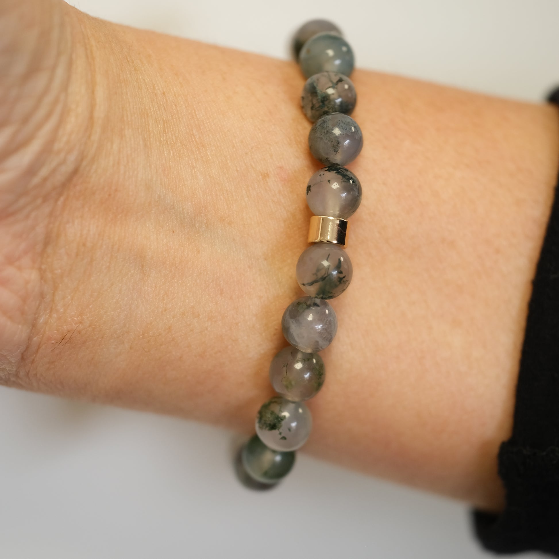 A moss agate gemstone bracelet worn on a model's wrist from behind