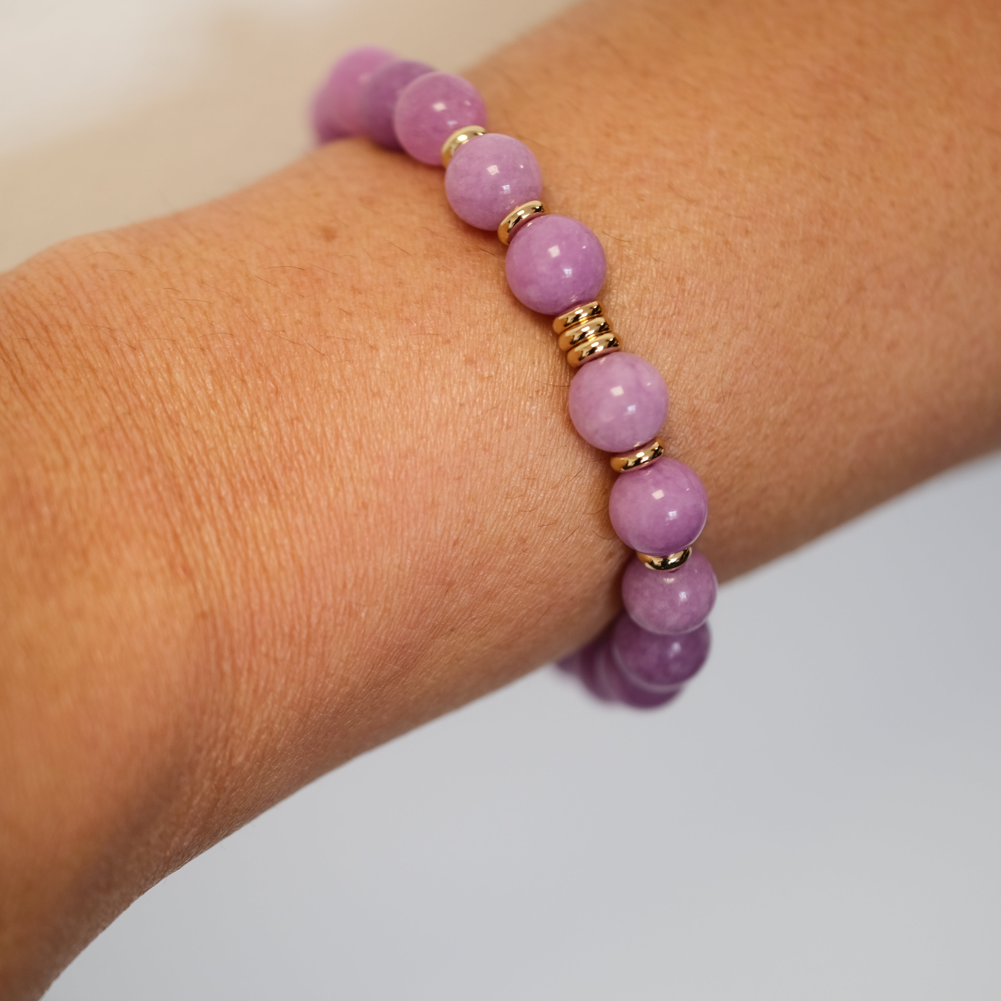 Lepidolite gemstone bracelet with gold accessories on a model's wrist