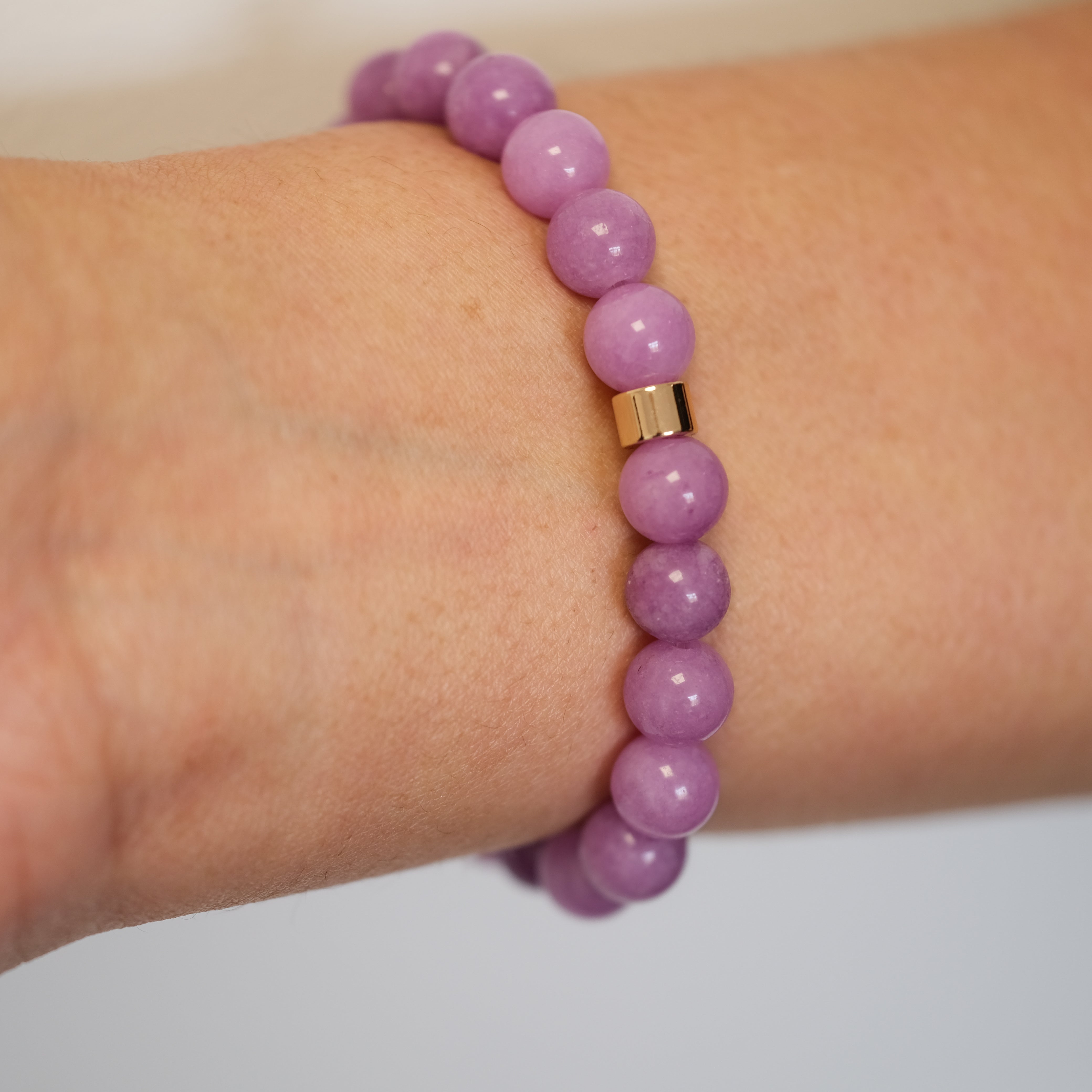 Lepidolite gemstone bracelet with gold accessories on a model's wrist from the back