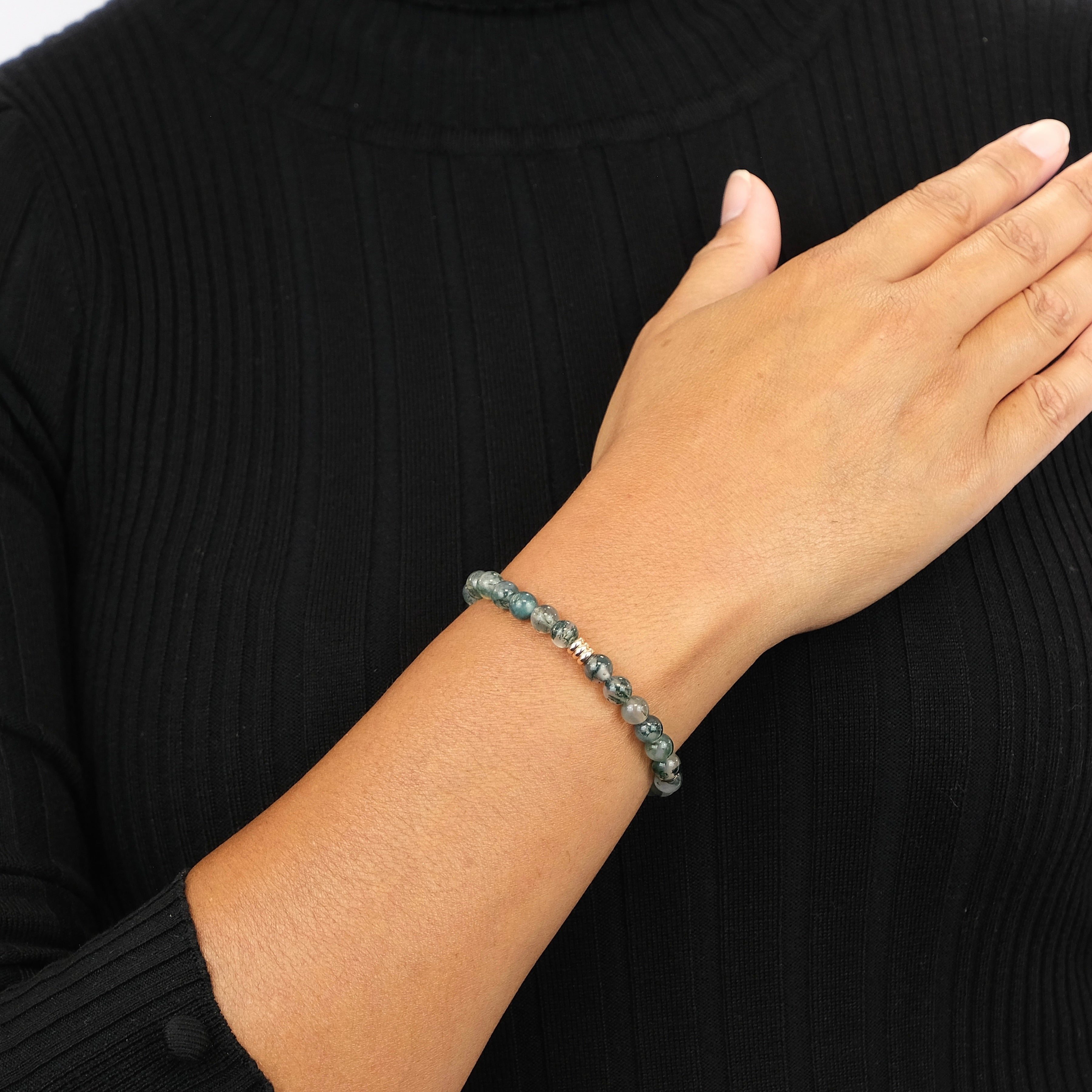 A model wearing a Moss agate gemstone bracelet in 6mm beads with gold accessories